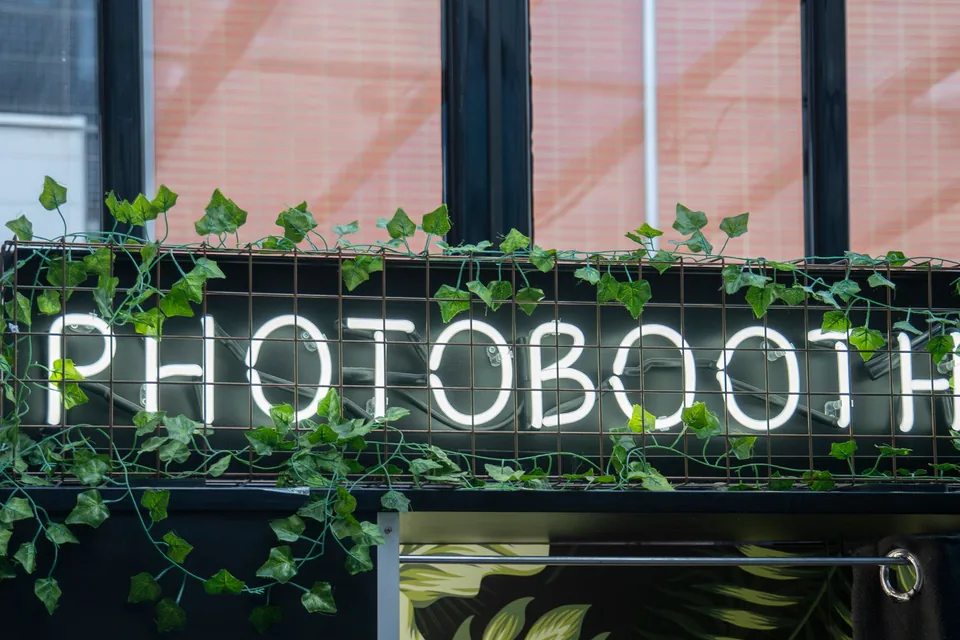 Enseigne néon « Photobooth » entourée de lierre, à l’entrée d’une soirée