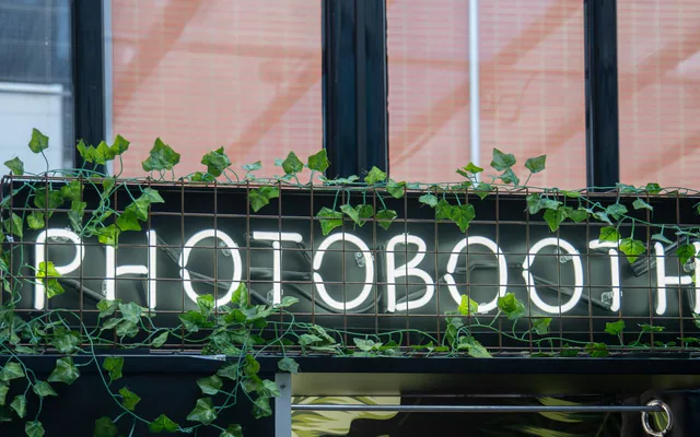 Enseigne lumineuse « Photobooth » entourée de lierre à l’entrée d’une soirée