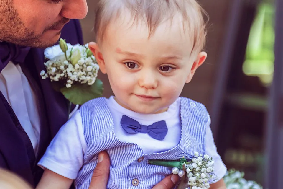 Bébé avec un nœud papillon dans les bras de son père, fleurs blanches au premier plan