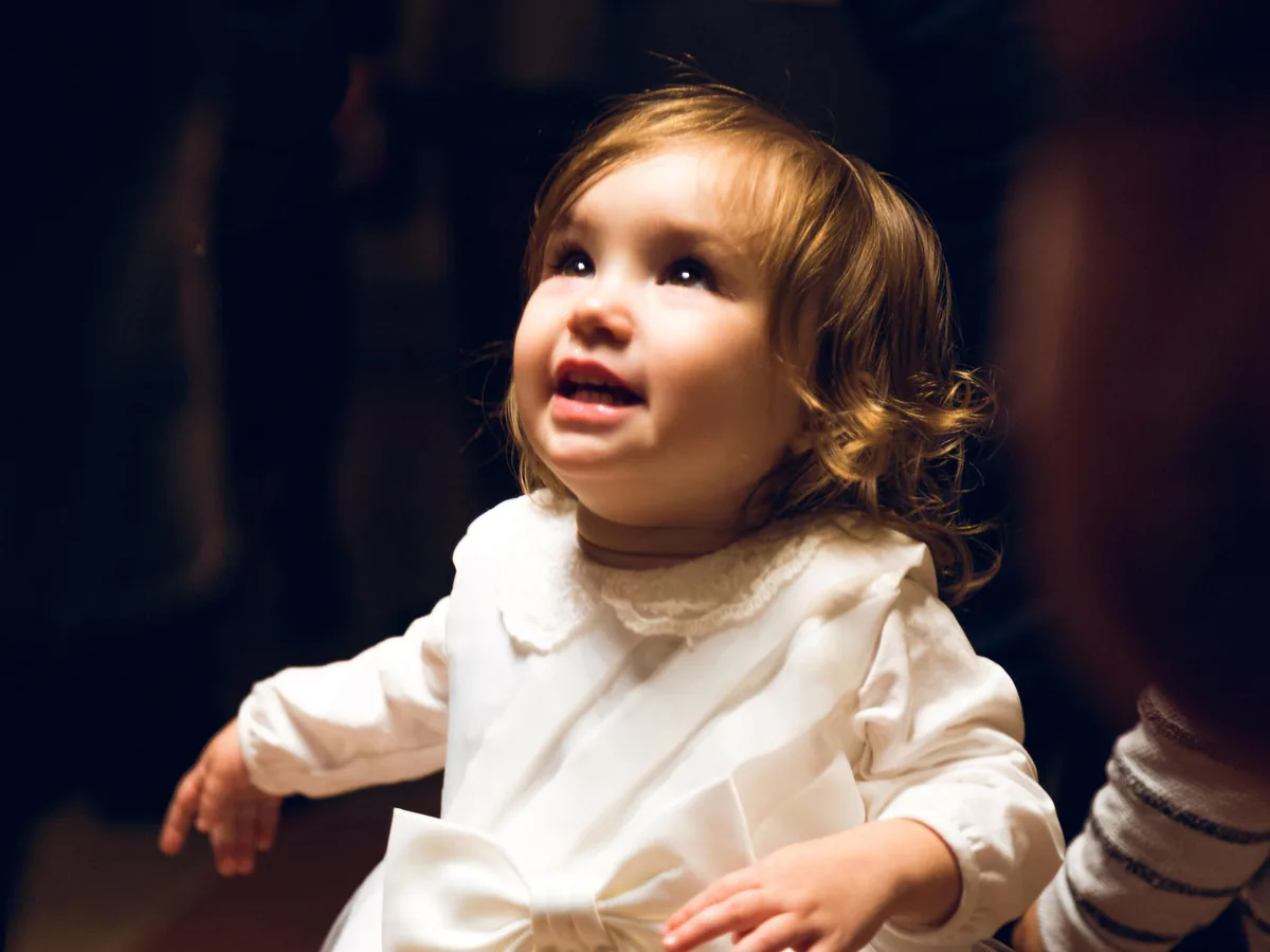 Petite fille en robe blanche de baptême qui lève les yeux, dans une lumière chaude