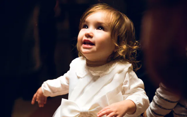 Petite fille en robe blanche de baptême qui lève les yeux, dans une lumière chaude