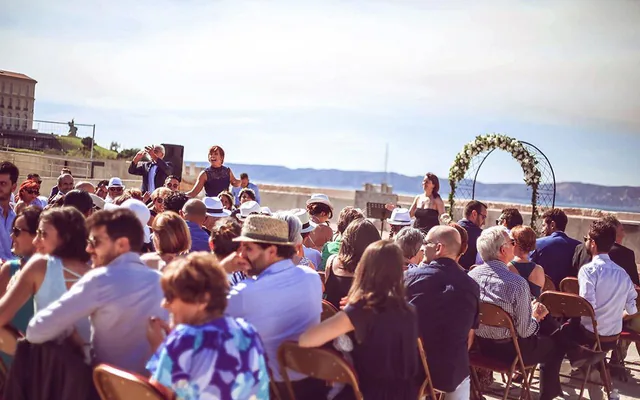 Invités assis devant une arche fleurie lors d’une cérémonie de mariage en plein air à Marseille