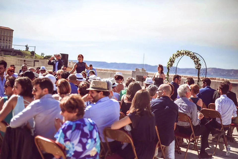 Invités assis devant une arche fleurie lors d’une cérémonie de mariage en plein air à Marseille
