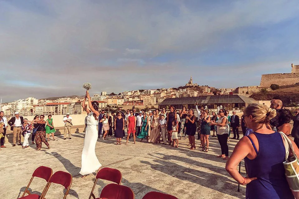 Mariés et invités sur un toit-terrasse au coucher du soleil, avec la ville de Marseille en fond