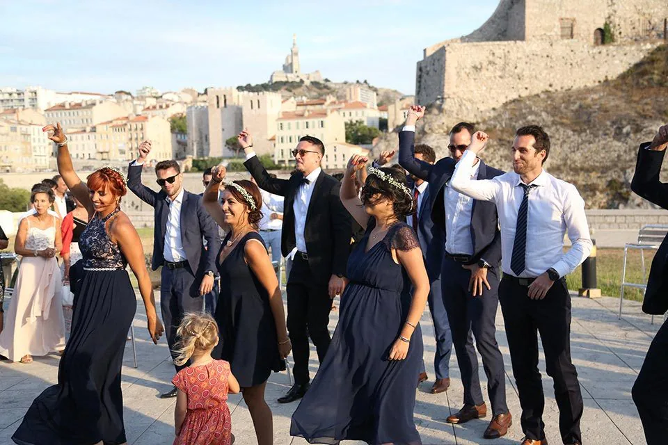 Invités qui dansent en plein air lors d’un mariage, avec Notre-Dame de la Garde en fond, à Marseille