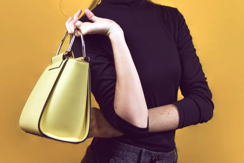 Femme en col roulé noir avec un sac jaune, sur fond jaune assorti, au studio à Marseille