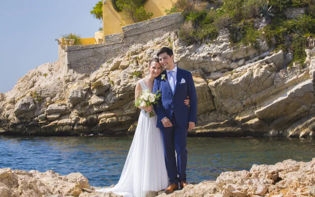 Couple de mariés au bord de l’eau dans une calanque de Marseille, falaise et bastide en arrière-plan