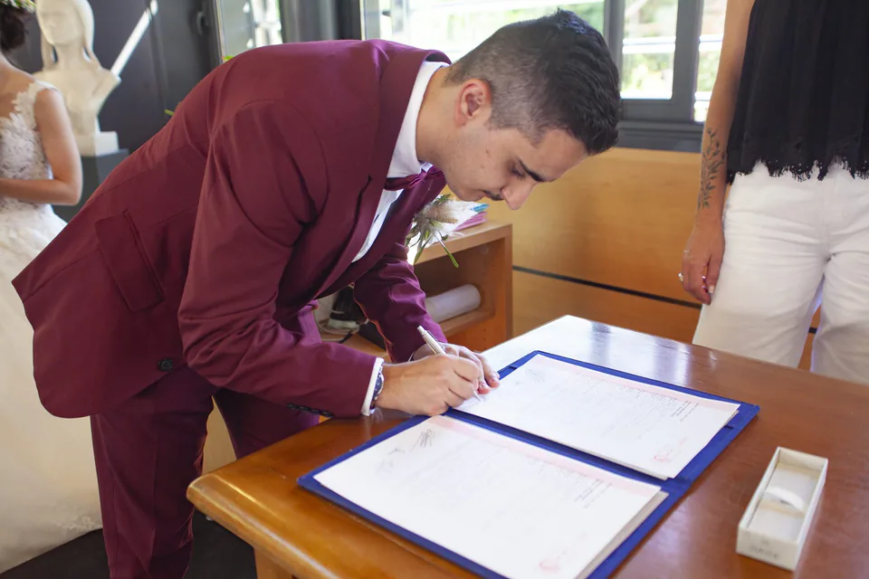 Marié en costume bordeaux qui signe le registre à la mairie, mariage à Marseille