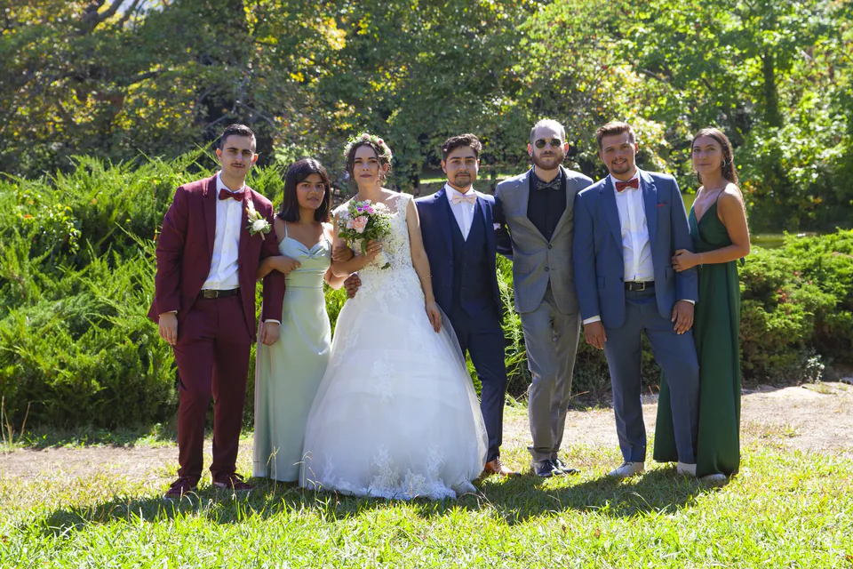 Photo de groupe de mariage dans un parc en plein soleil de midi, ombres marquées sur les visages